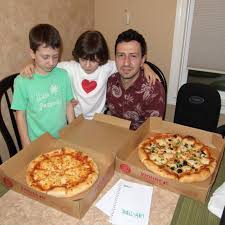 A historical photograph, rich in bitcoin nostalgia, showing Laszlo Hanyecz holding one of his children, with the other nearby, and the two Papa John's pizzas purchased for 10,000 BTC on a table.